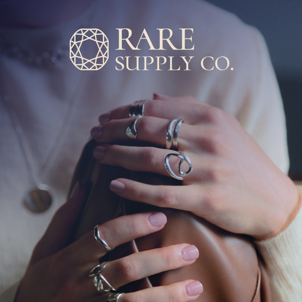 Rare Supply co. primary logo is offwhite layered on top of an image with a woman wearing lots of rings and jewelry showcasing their brand identity in the best light
